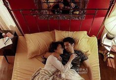 a man and woman laying on a bed in the middle of a room with red walls