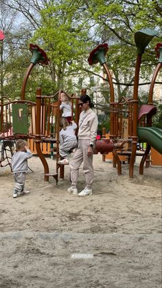 a woman and two children standing in front of a playground