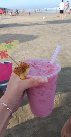 a person holding up a pink drink on the beach