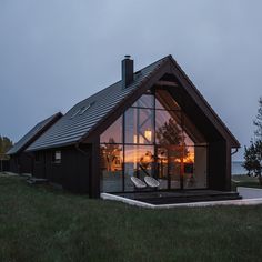 a house with large windows sitting on top of a lush green field next to the ocean