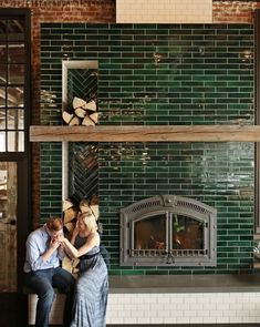 two people sitting on a bench in front of a fireplace