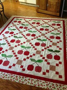 a quilted table topper with cherries and leaves on it, sitting on a wooden floor