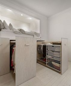 an open closet in the middle of a room with white walls and wood floors, filled with clothes