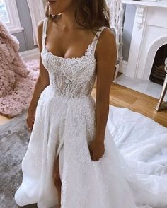 a woman wearing a white wedding dress standing in front of a fireplace with her legs crossed