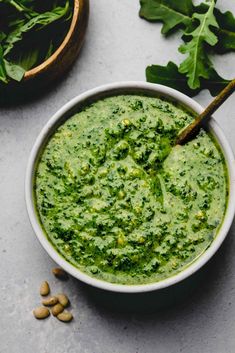 a white bowl filled with pesto next to some green leaves and other food items