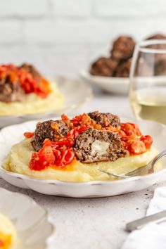 two plates with meatballs and mashed potatoes on them next to some glasses of wine