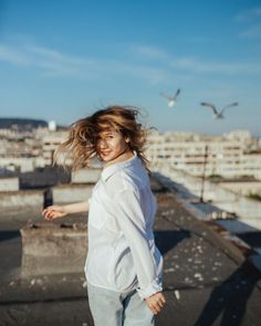 a woman with her hair blowing in the wind on top of a roof near seagulls