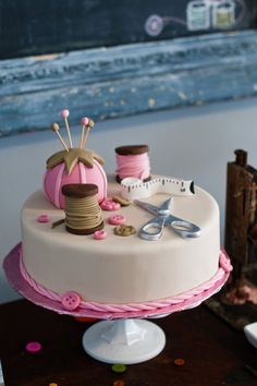 a white cake with pink icing and spools of thread on it, sitting on a table