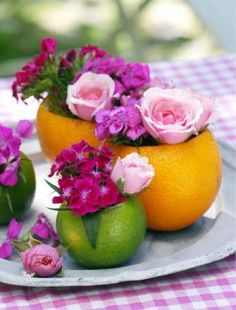 three oranges with pink flowers in them on a plate next to some green apples