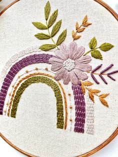 a close up of a embroidery on a hoop with a flower and a rainbow in the middle