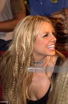 a woman with long blonde hair smiling and looking to the side in front of other people