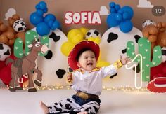 a baby wearing a cowboy hat sitting on the floor in front of balloons and decorations