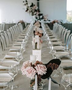 a long table is set with white and pink flowers, wine glasses, and place settings