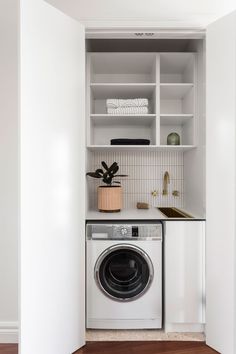 a washer and dryer in a small room with white walls, wood flooring and open shelving