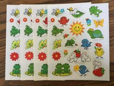 four sheets of stickers with different cartoon animals and flowers on them, sitting on a wooden surface