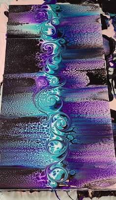 an abstract painting with blue and purple colors on black paper, sitting on top of a table