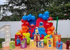 an outdoor birthday party with balloons and sesame street characters on the table, in front of a white fence