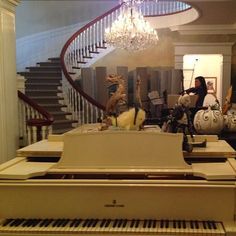 a grand piano is in the middle of a room with stairs and chandelier