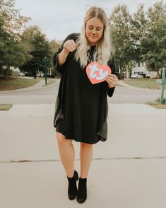 a woman standing on the sidewalk holding up a heart