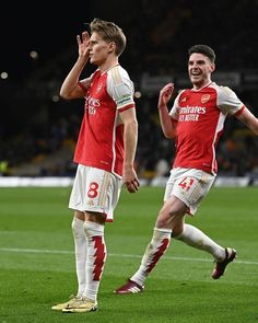 two soccer players are walking on the field and one has his hand up to his mouth