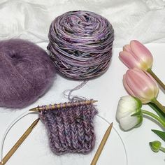 two skeins of yarn next to a ball of knitting needles and tulips