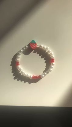 a white bracelet with red beads and a strawberry on the end is sitting on a table