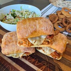 two sandwiches cut in half on a cutting board with onion rings and coleslaw