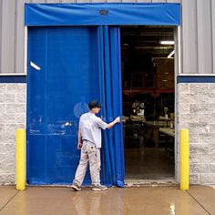 a man standing in front of a blue door with his hand on the open curtain