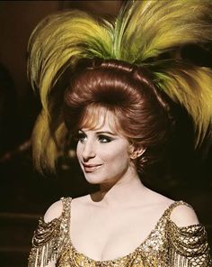 a woman with red hair wearing a gold dress and yellow feathers on top of her head