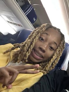 a man with dreadlocks sitting on an airplane pointing at the camera and smiling