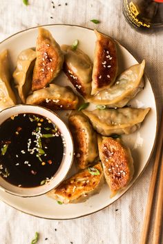 a white plate topped with fried dumplings next to dipping sauce and chopsticks