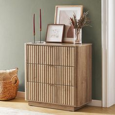 a wooden dresser sitting next to a green wall with pictures and candles on top of it