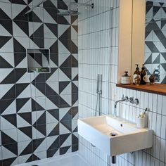 a bathroom with black and white tiles on the wall, sink and shower stall area