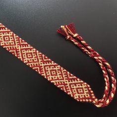 a red and white braided bracelet on a black surface with a tassel hanging from it