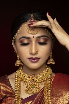 a woman wearing gold jewelry and holding her hands up to her head