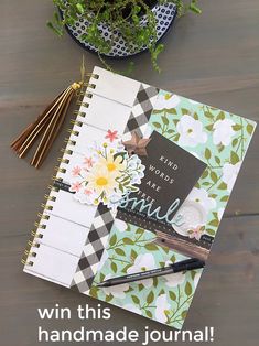 an open journal sitting on top of a wooden table next to a potted plant