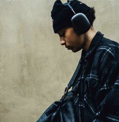 a young man wearing headphones looking at his cell phone while standing in front of a wall