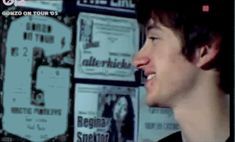 a young man standing in front of a wall with posters on it's side