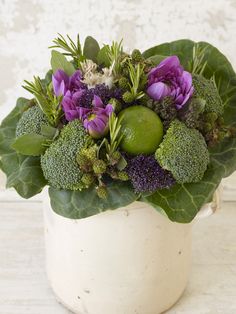 a white vase filled with lots of different types of flowers and greenery on top of a wooden table