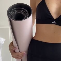 a woman in black sports bra holding a pink yoga mat and rolled up exercise mats