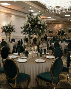 a banquet room set up with green velvet chairs and white tablecloths, tall centerpieces filled with flowers and greenery