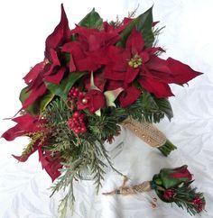 a bouquet of red poinsettias and greenery on a white cloth background