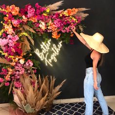 a woman standing in front of a neon sign with flowers and feathers on it,