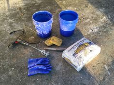 buckets and tools are sitting on the ground next to two blue plastic cups with handles