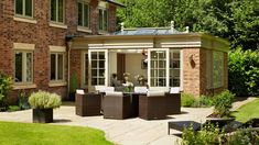 an outdoor patio with wicker furniture and potted plants on the ground in front of a brick building