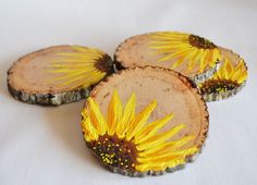 three sunflowers painted on wood slices sitting on a white tablecloth covered surface