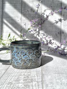 a blue mug sitting on top of a wooden table next to a purple flower bush