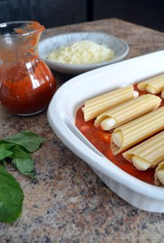 some pasta and sauce in a white dish on a counter next to a small glass jar