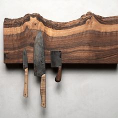 three knives are hanging on a wall with some wood and metal tools attached to it