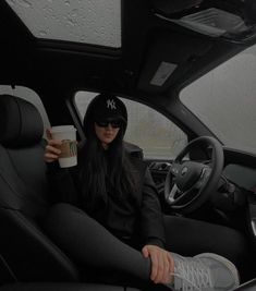 a woman sitting in the driver's seat of a car holding a coffee cup